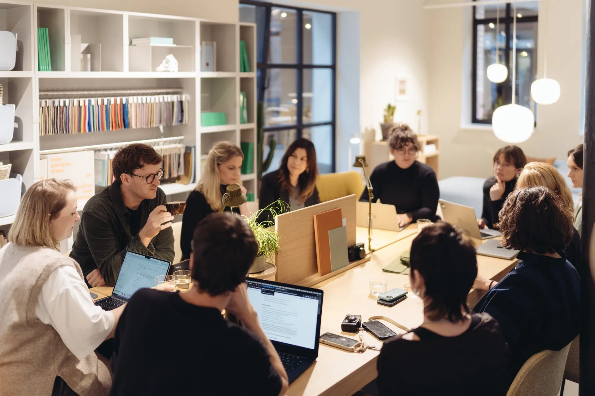 A workshop group at a long table in a showroom, several people working on laptops, bookshelves in the background