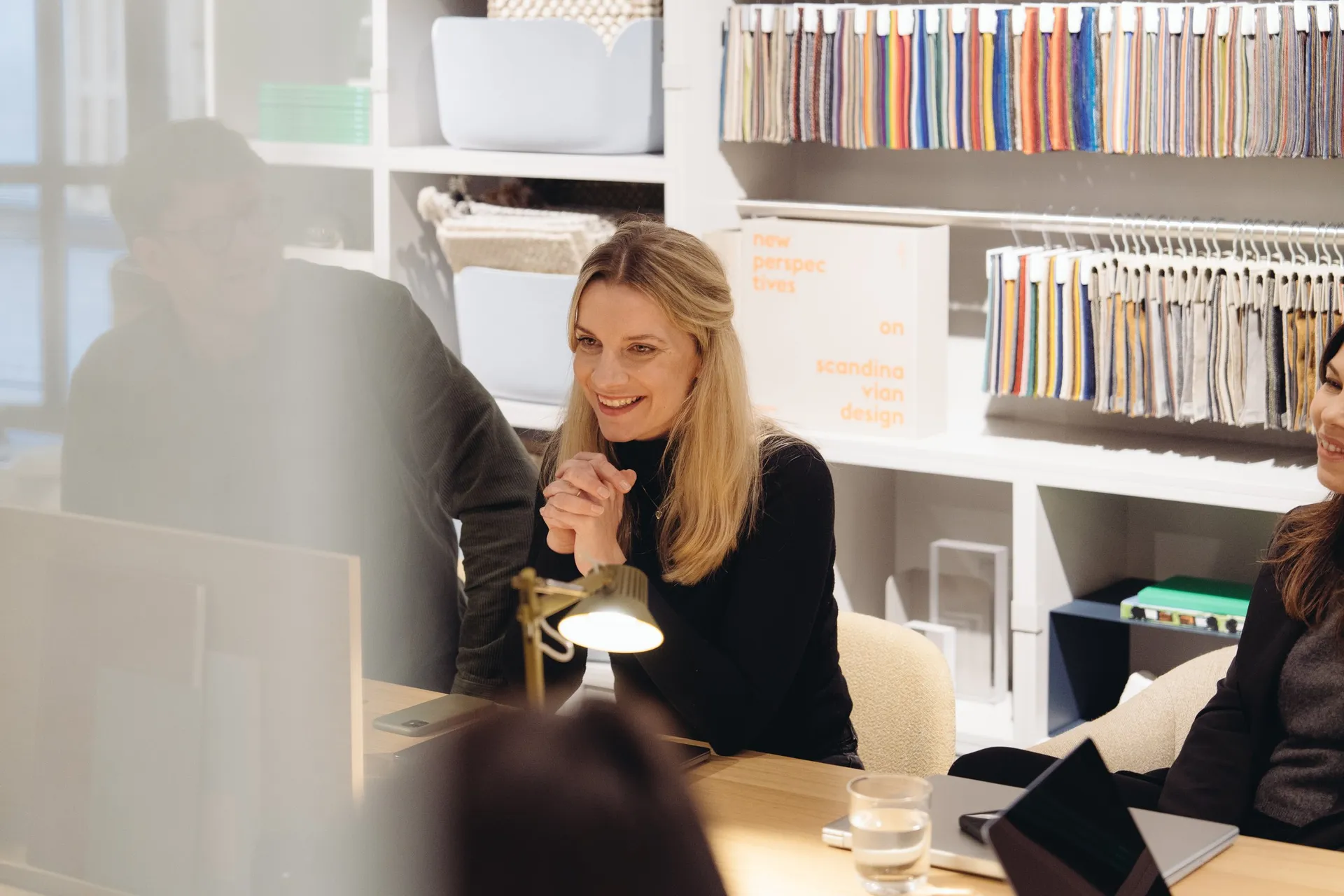 Eine Frau lacht im Gespräch in einem Showroom, im Hintergrund ein Regal mit Büchern