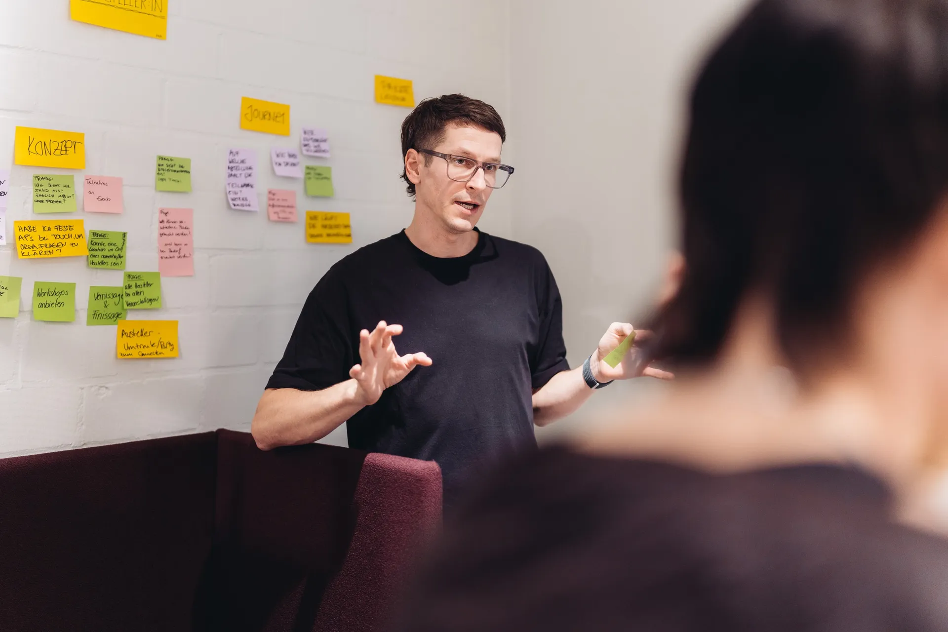 Michael Rahmfeld erklärt im Workshop vor einer Wand mit Haftnotizen, im Vordergrund unscharf eine Teilnehmerin